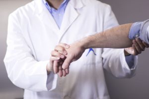 A doctor holding a patient's arm and testing their lower limb for a broken wrist.