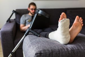 PERSON WITH BROKEN LEG AND CRUTCHES SEARCHING FOR PERSONAL INJURY SOLICITORS ON LAPTOP AFTER A TRAIN STATION INJURY.