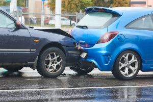 A black car crashing into the back of a blue car causing vehicle damage
