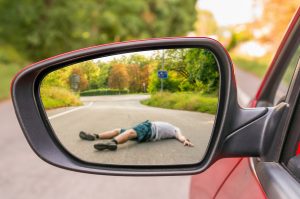 A man lying in the road being views through the reflection of a car's side view mirror